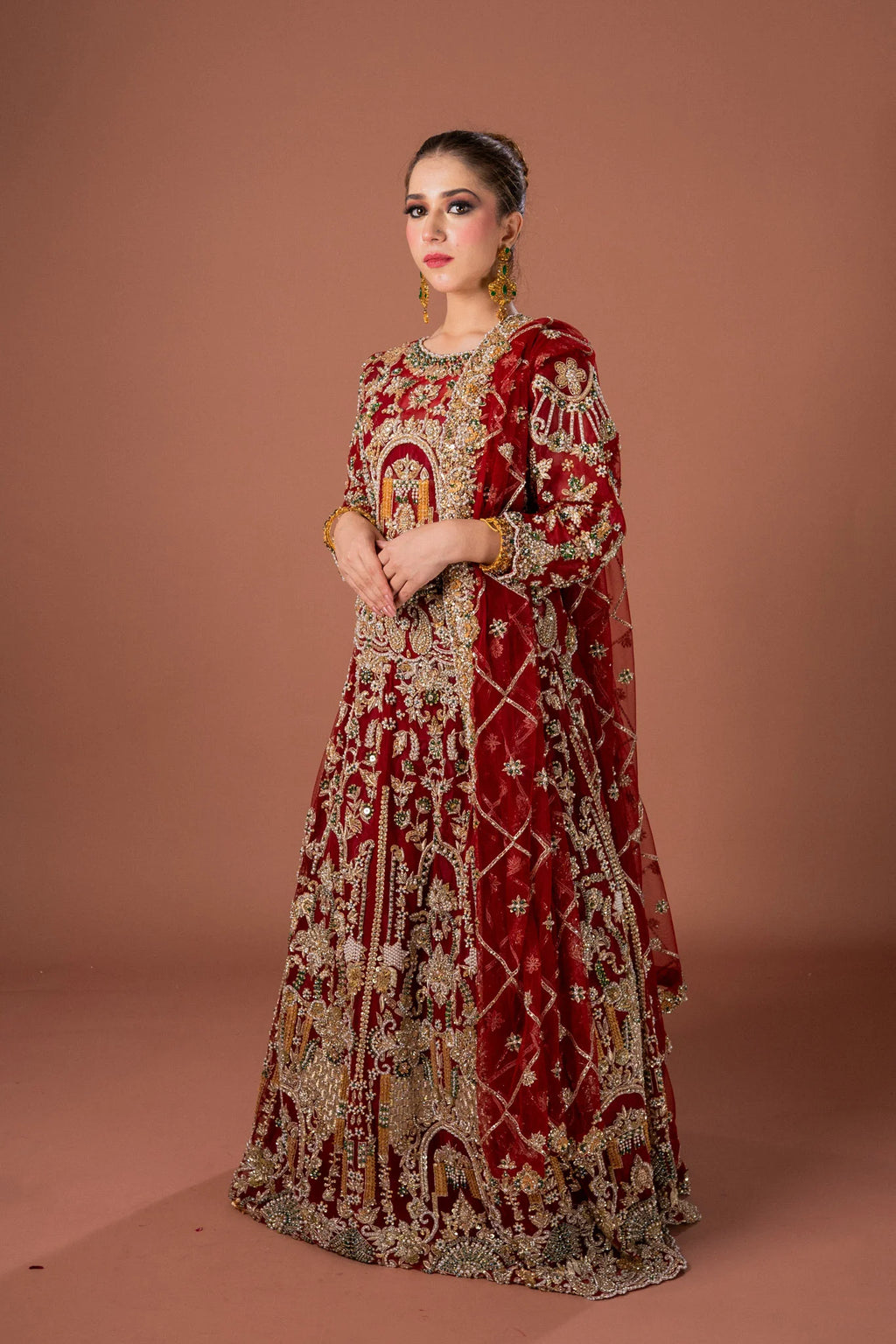 A woman wearing a traditional red lehnga set with detailed gold, silver, and multicolor embroidery, including a net dupatta and a blouse.