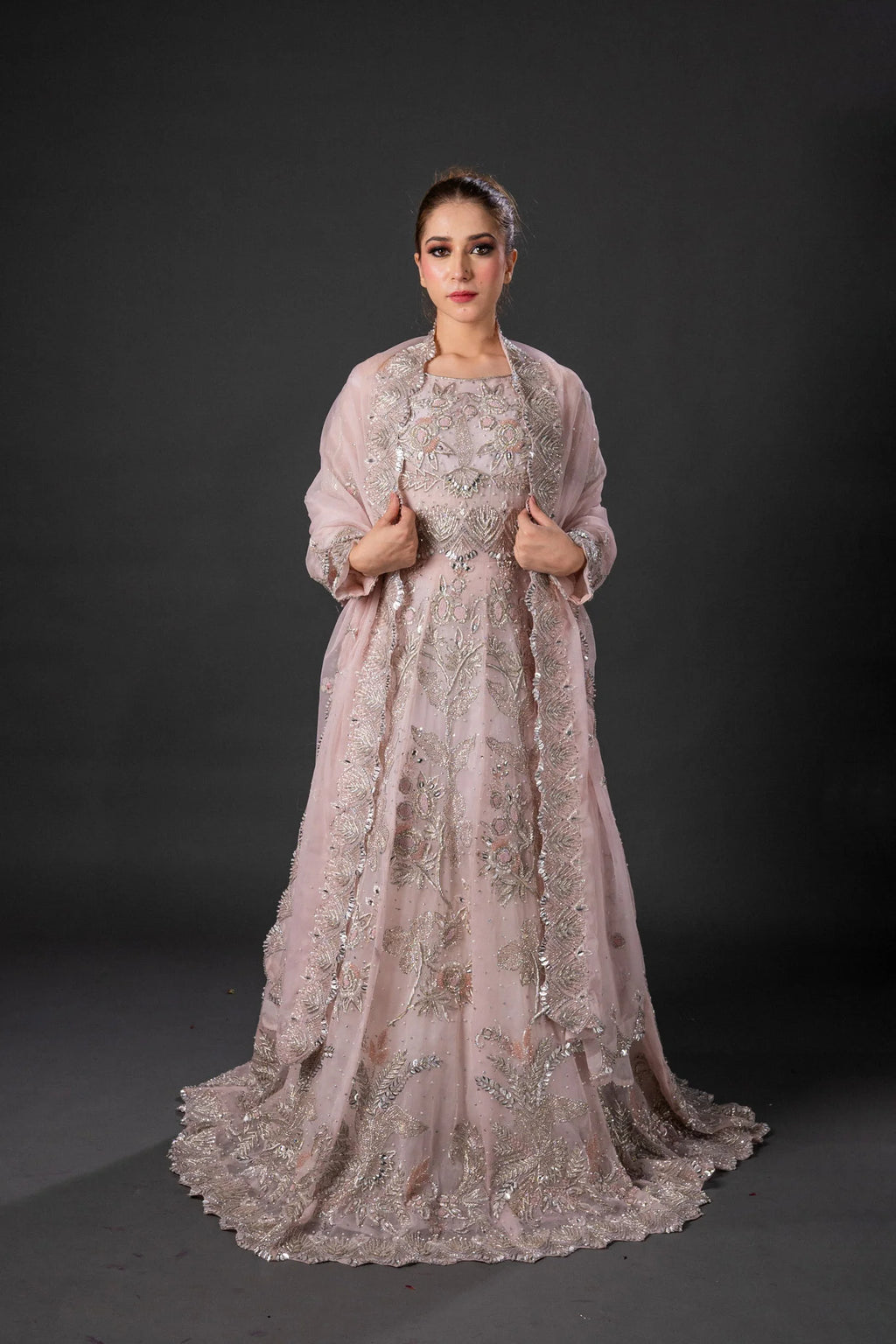 A woman wearing a traditional pink maxi set with embroidery and a dupatta lehnga blouse, against a neutral background.