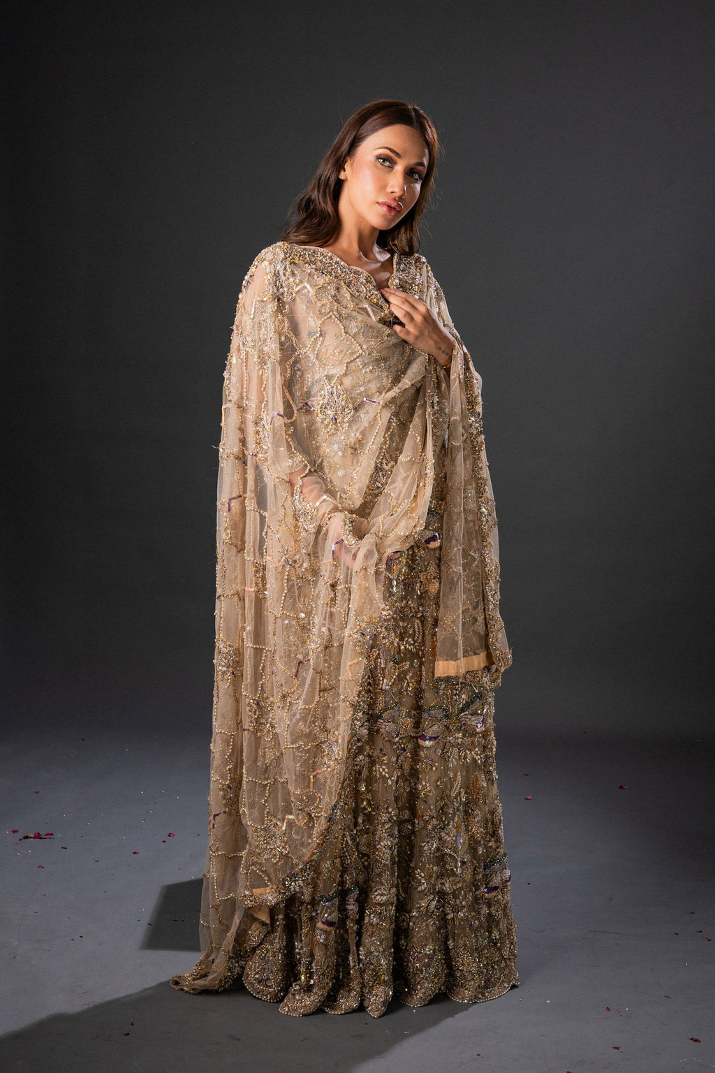 A woman wearing a traditional, embellished, golden maxi dress with a dupatta, featuring intricate front embroidery and a sweeping tail.