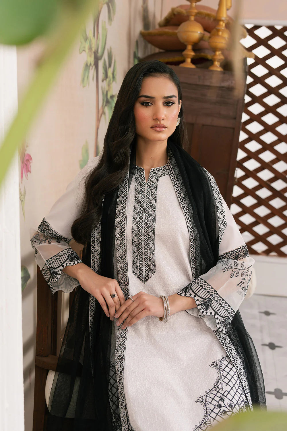Woman wearing a traditional outfit with black and white embroidery in an indoor setting.