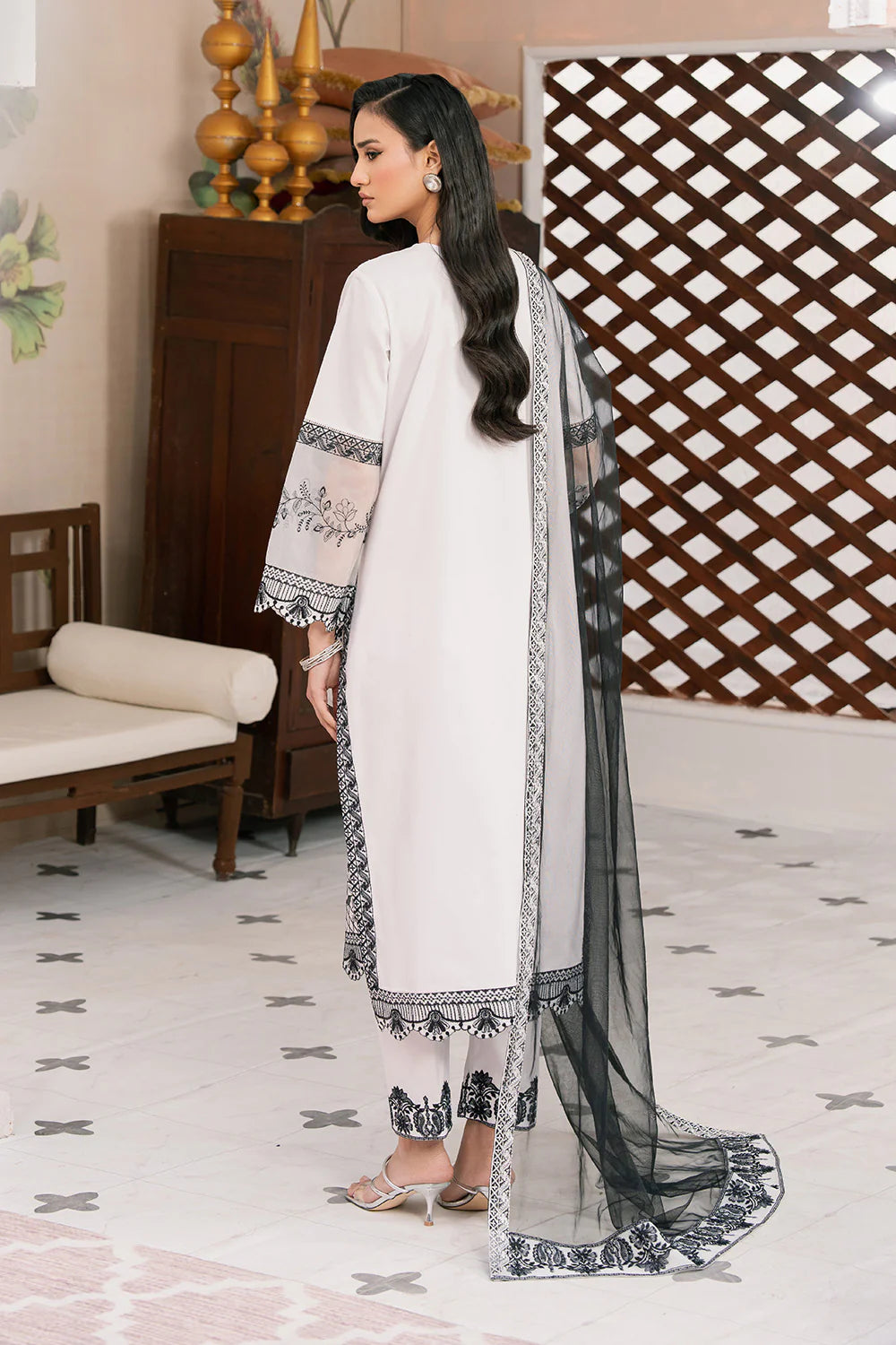 Woman in a white and black traditional outfit with a sheer dupatta in a room.