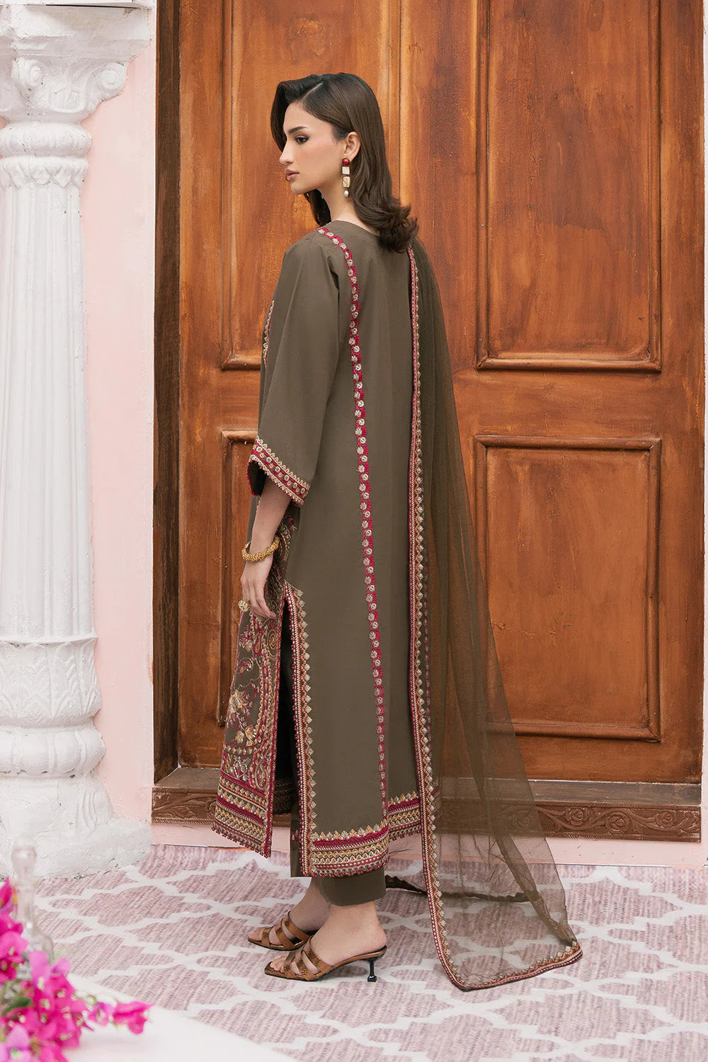 Woman wearing a long, dark green embroidered dress with a sheer overlay in front of a wooden door.