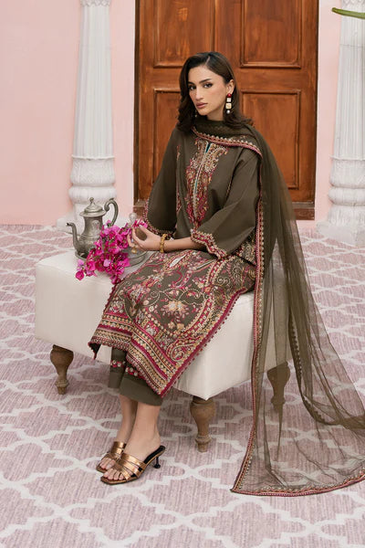 Woman in traditional embroidered outfit sitting on a white stool with pink floral arrangement.