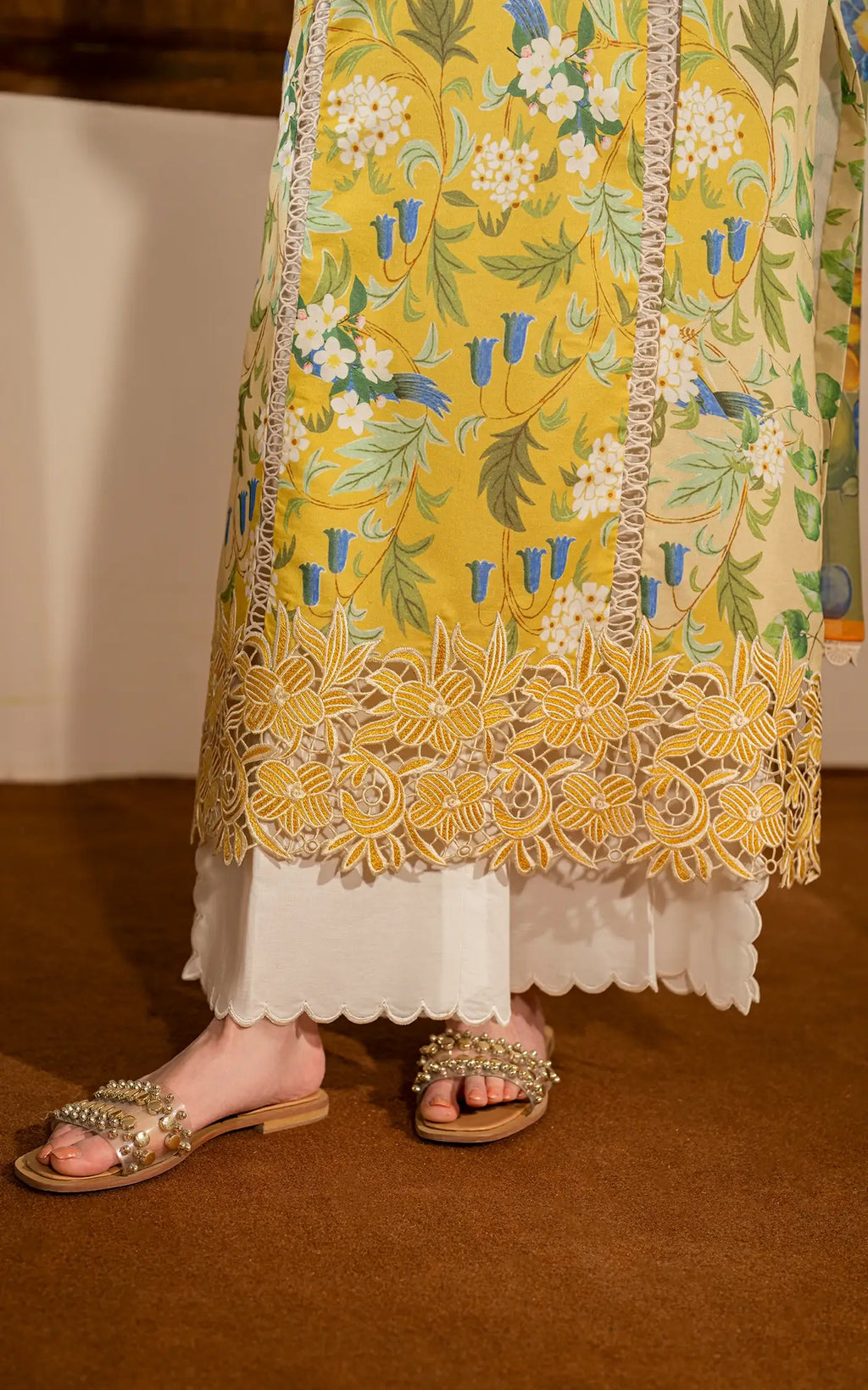 Yellow floral embroidered kurta with white pants and sandals on a brown floor.