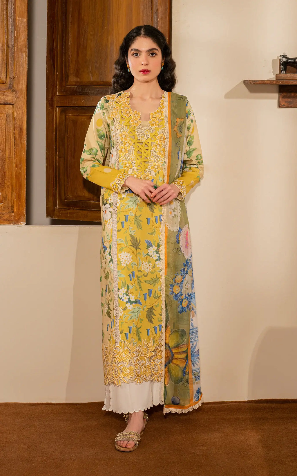 Woman wearing a yellow floral dress with a matching dupatta in a minimal indoor setting.