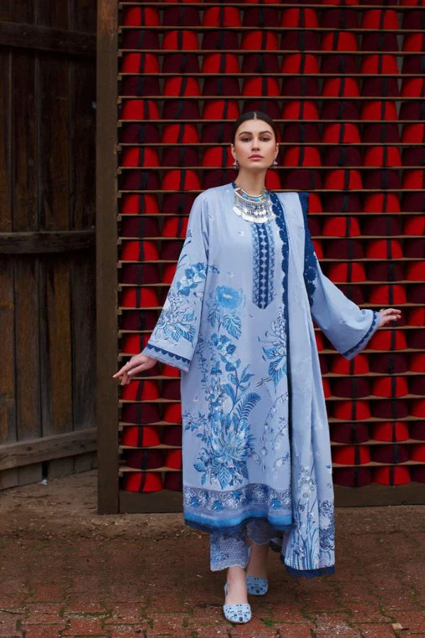 A woman modeling a light blue traditional embroidered kurta set with intricate blue floral patterns, standing in front of a red slatted wall.