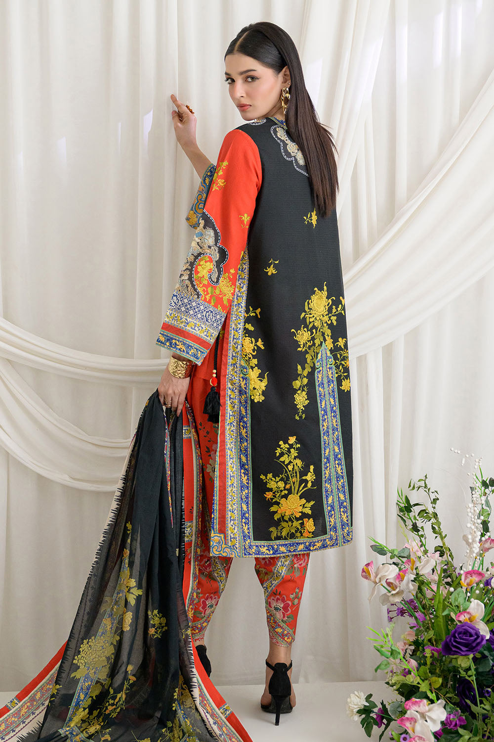 Woman wearing a traditional outfit with floral patterns in a white room with flowers.