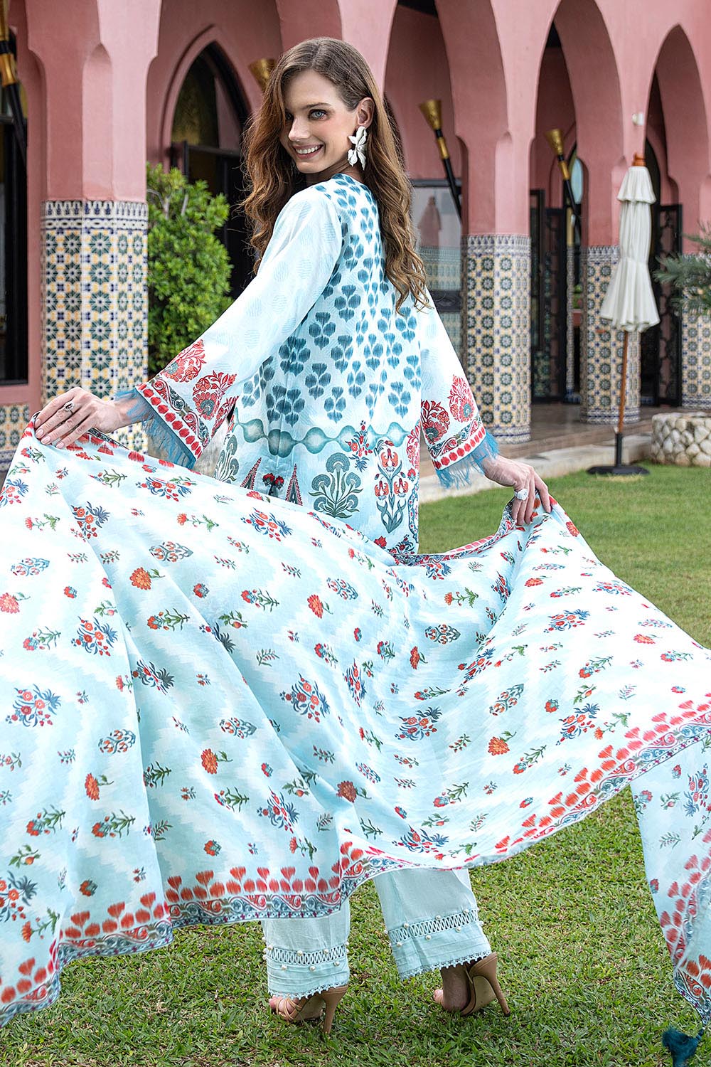 Woman in a floral dress standing outdoors with a decorative building in the background