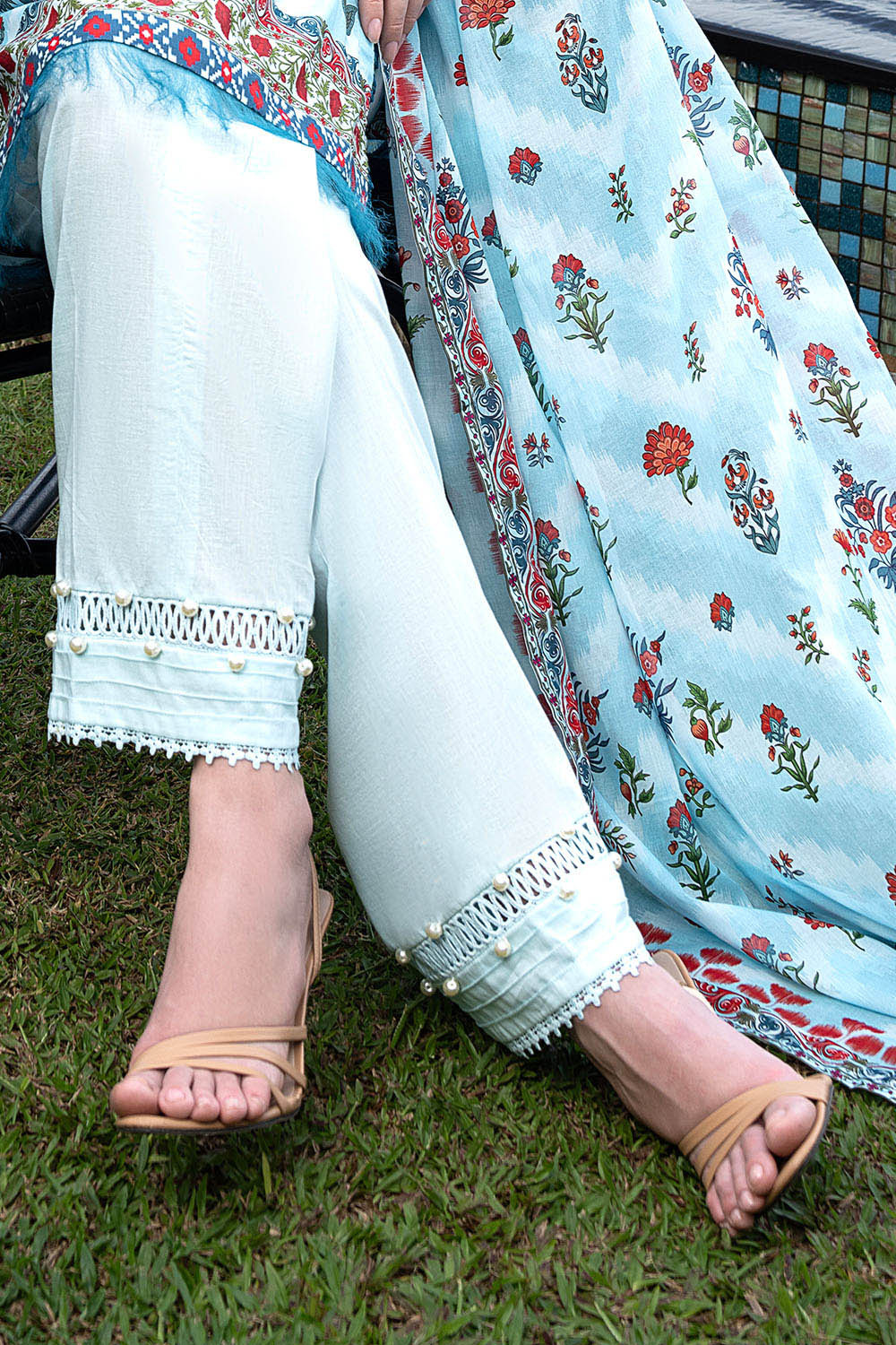Person wearing light blue pants with white lace cuffs and a floral shawl on grass.