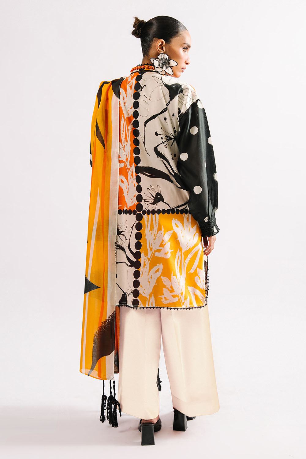 Woman wearing a black and white patterned outfit with a long orange scarf on a white background
