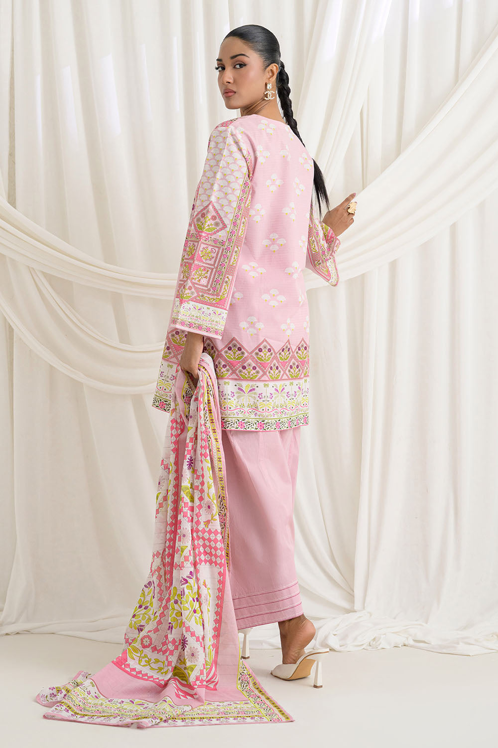 Woman wearing a pink traditional outfit with a matching dupatta against a white curtain background