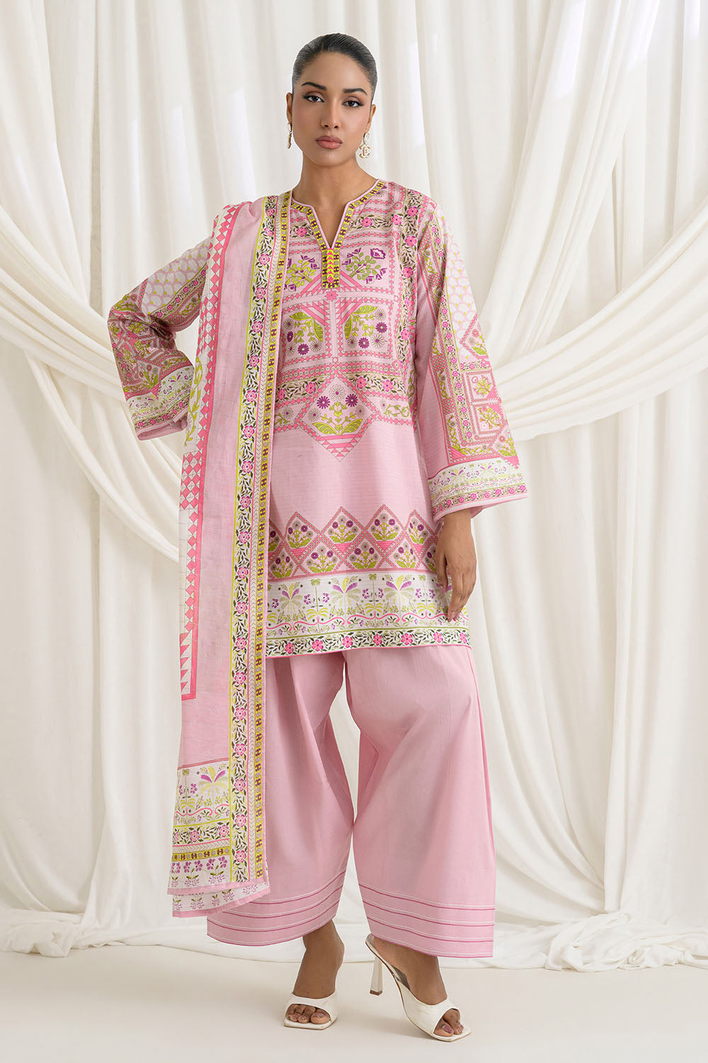 Woman wearing a pink traditional outfit with intricate patterns against a white curtain background