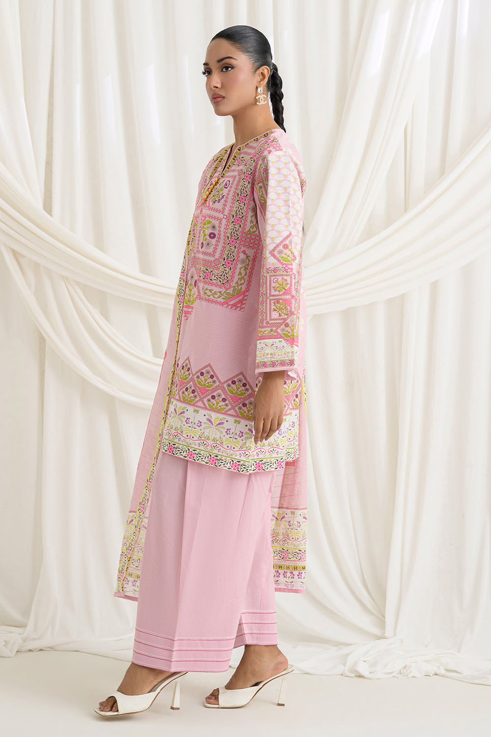 Woman wearing a pink embroidered traditional outfit against a white curtain background