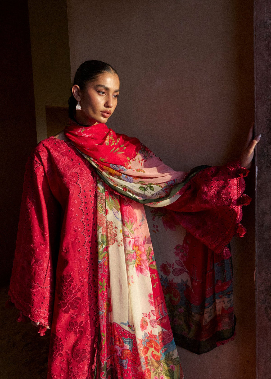 Woman wearing a vibrant red and floral traditional outfit against a plain background