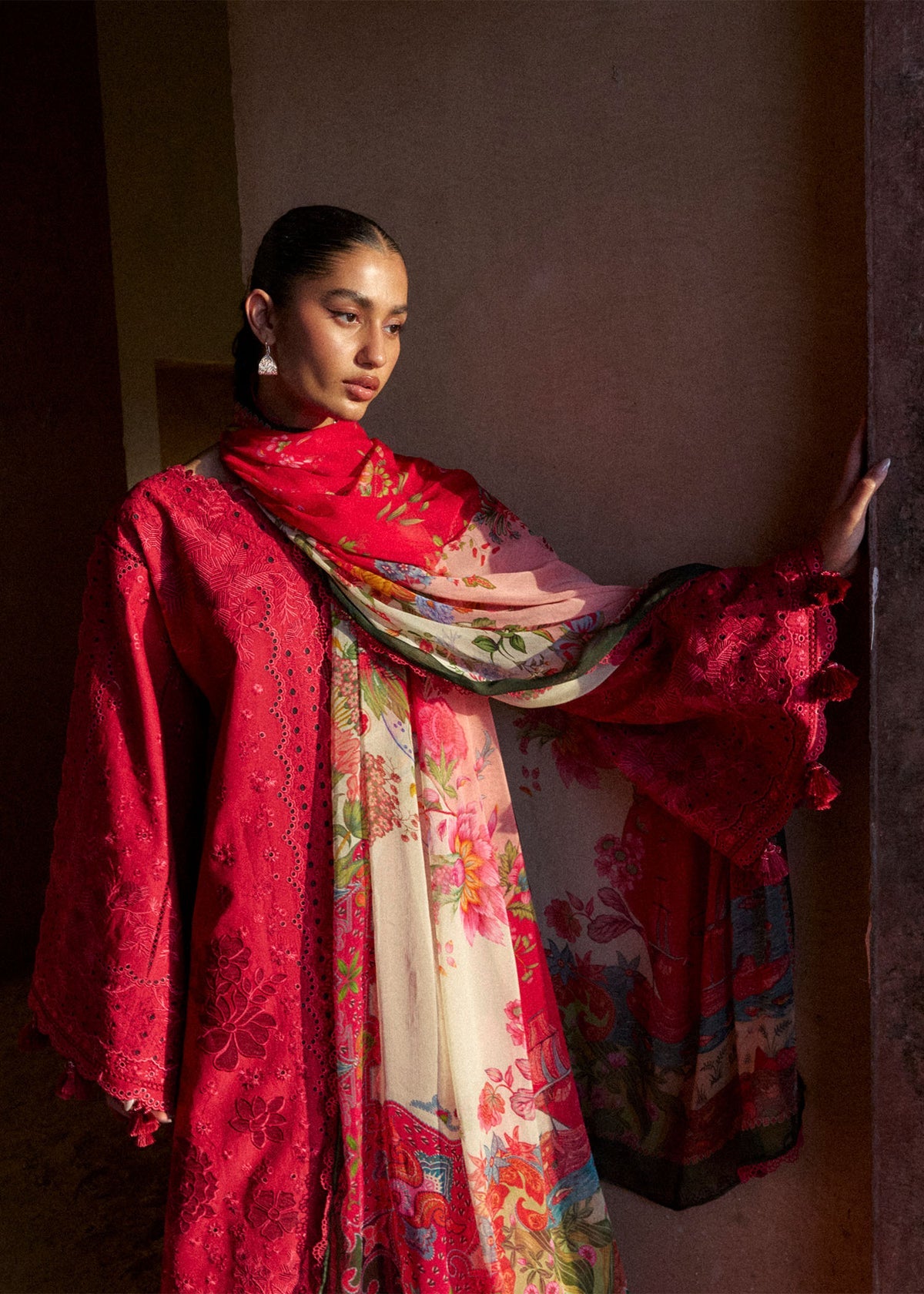 Woman wearing a vibrant red and floral traditional outfit against a plain background