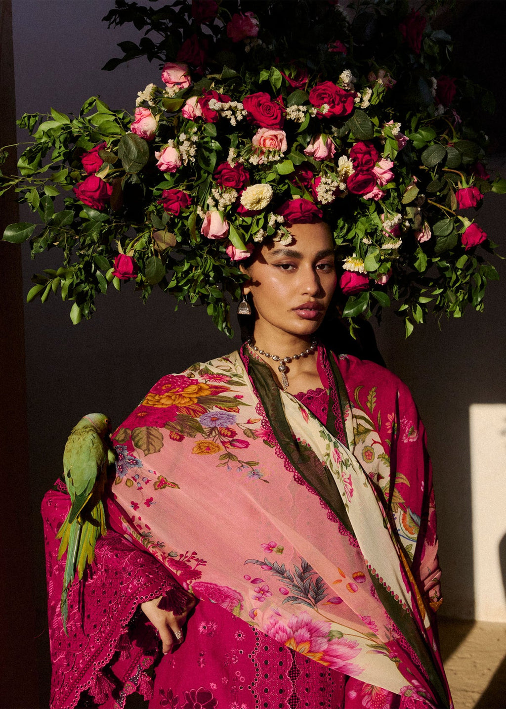 Woman wearing a vibrant floral headpiece and colorful outfit with a parrot on her shoulder.