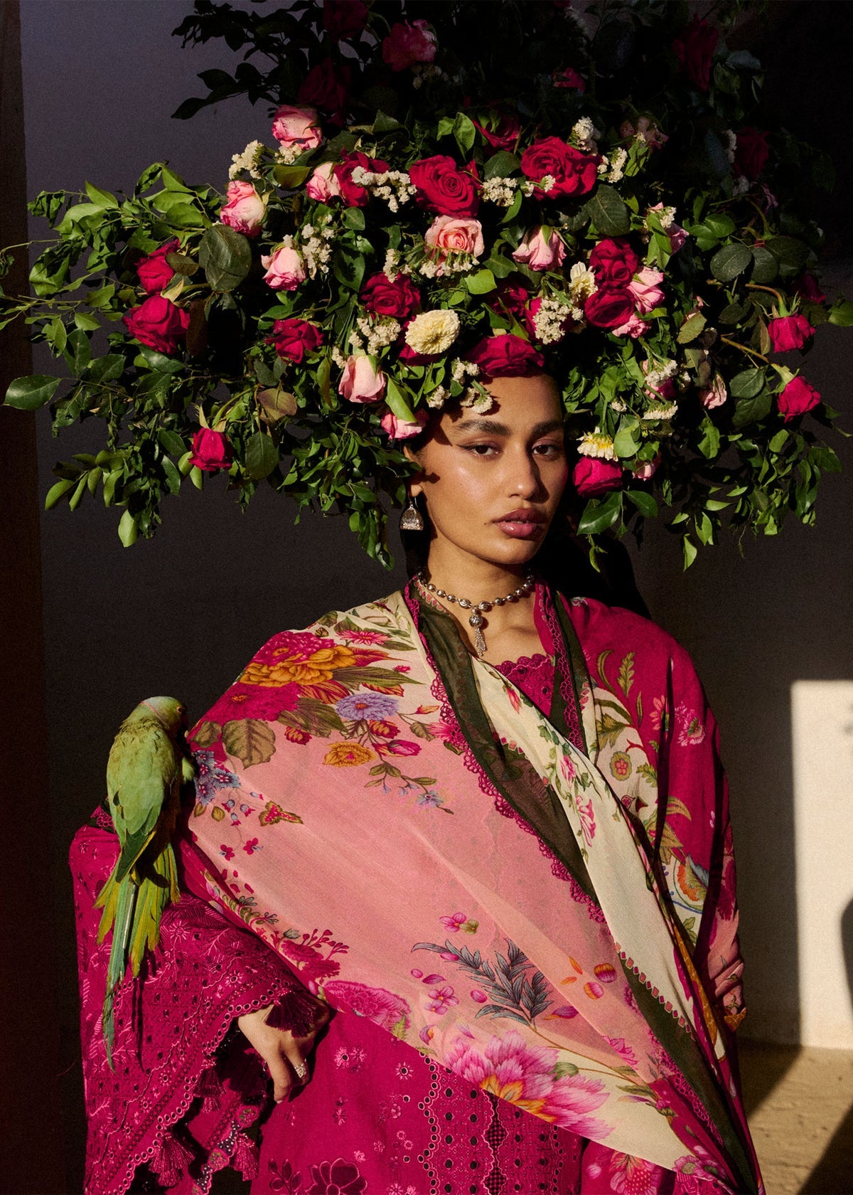 Woman wearing a vibrant floral headpiece and colorful outfit with a parrot on her shoulder.