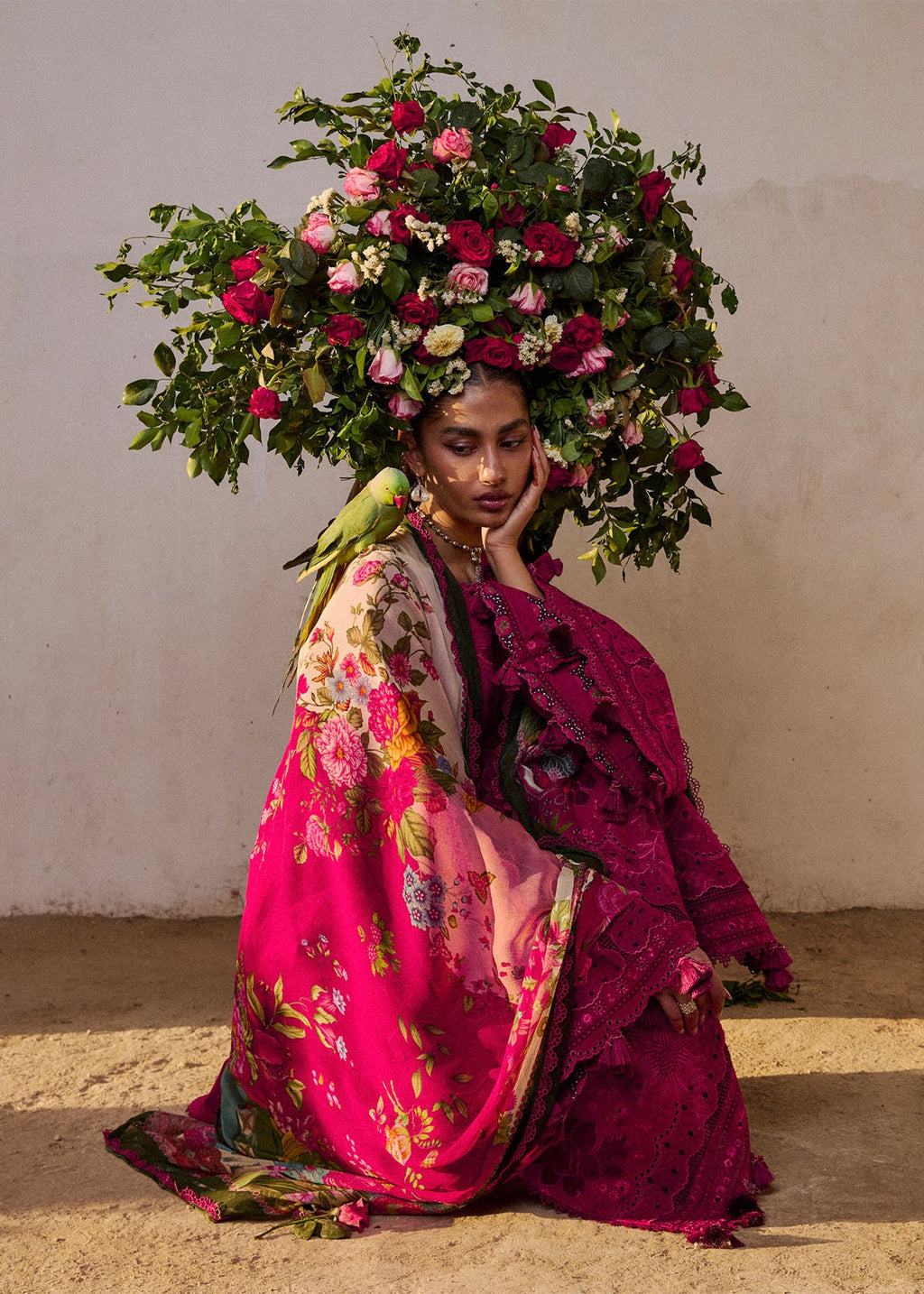 Woman in a vibrant pink and green traditional outfit with a floral headpiece against a plain background