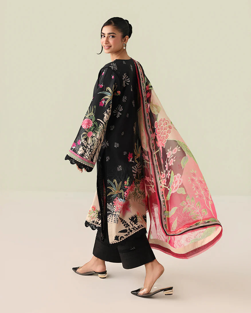 Woman wearing a black floral outfit with a pink and beige dupatta on a light green background