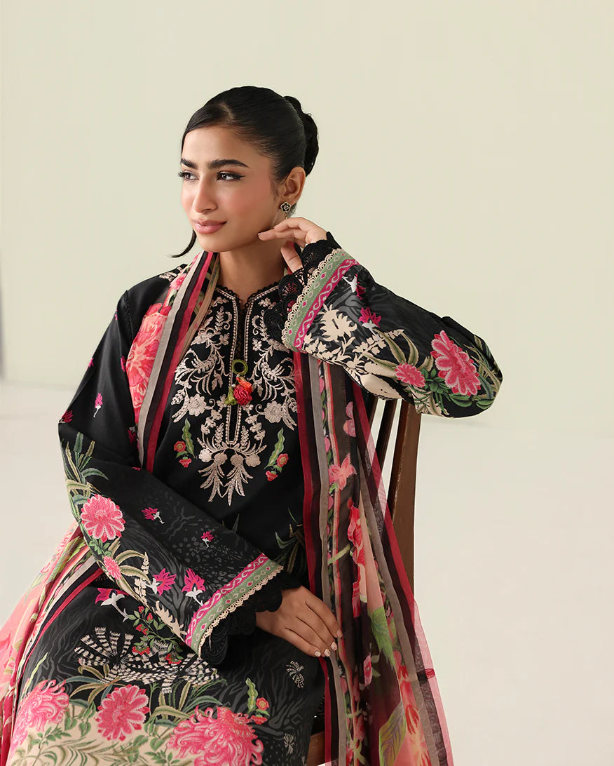 Woman wearing a black embroidered traditional outfit with pink and green details on a light background