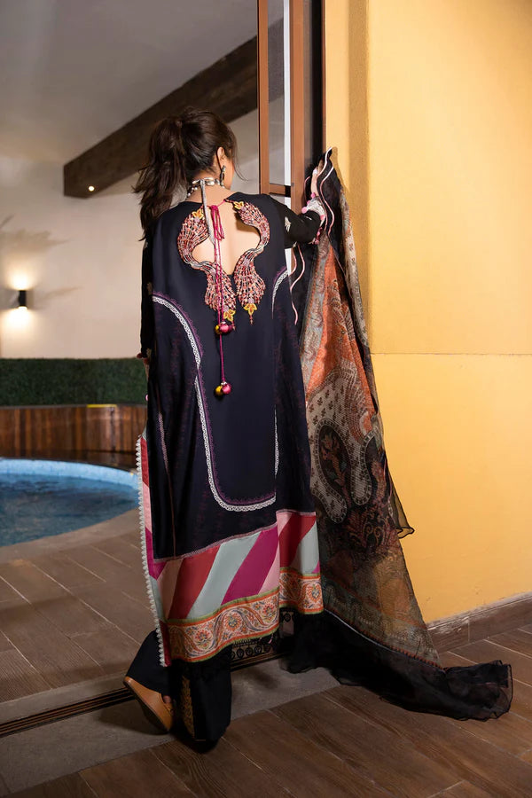 A woman stands with her back to the camera wearing a black traditional outfit with ornate multicolor embroidery and a patterned dupatta, in an indoor setting with a pool and warm yellow walls.