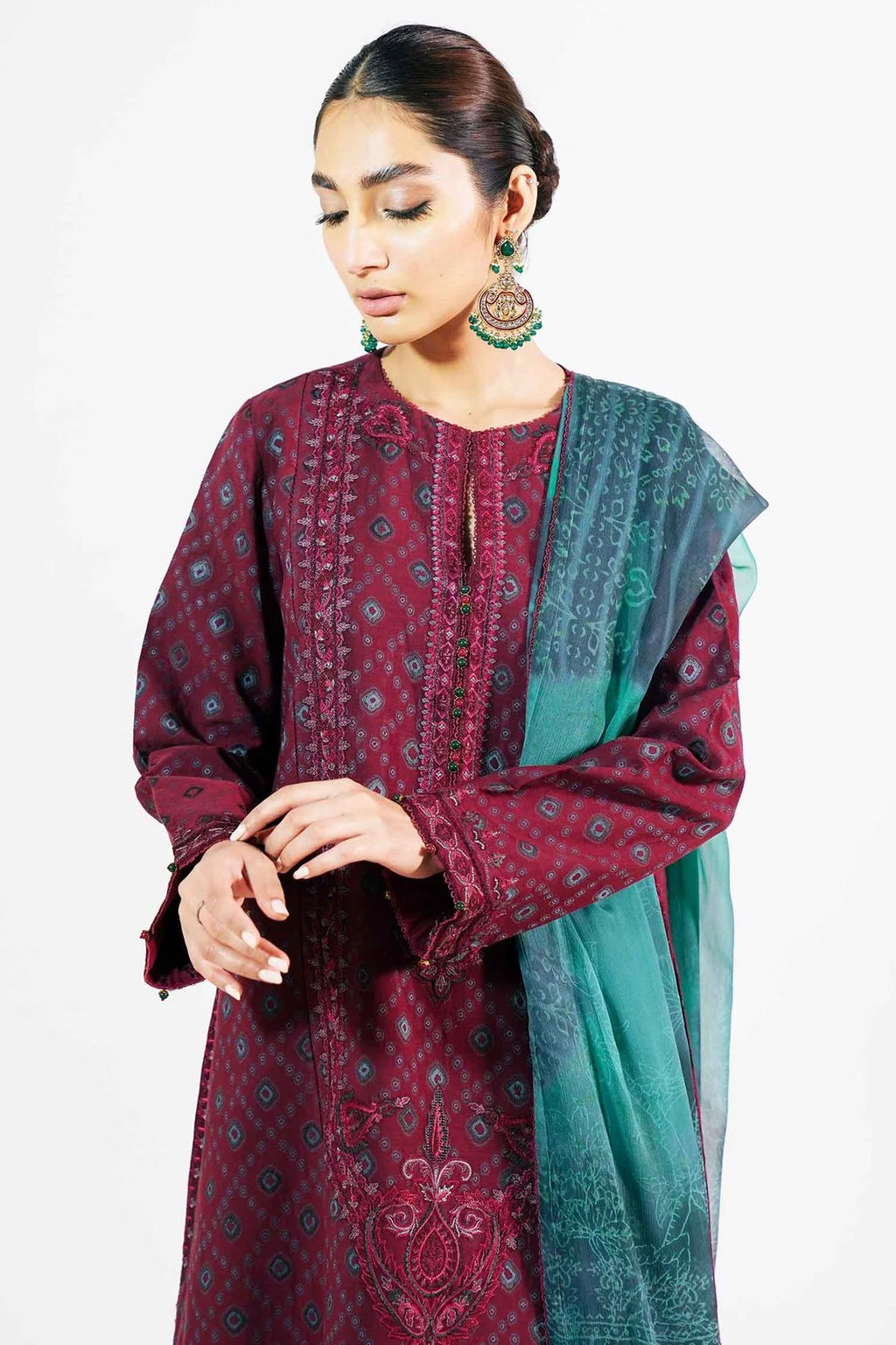 A woman modeling a traditional three-piece salwar kameez suit in deep maroon with blue geometric patterns, paired with a teal and maroon printed dupatta, set against a plain white background.