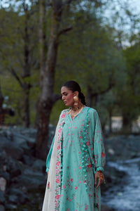 Woman in a teal floral outfit standing in a natural setting with trees and rocks.