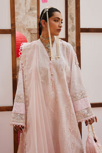Woman wearing a light pink embroidered traditional outfit with jewelry, standing indoors.