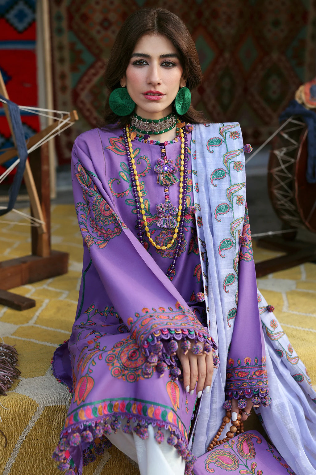 Woman wearing a purple embroidered outfit with a white dupatta in a decorative setting.