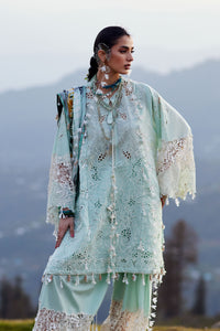 Woman in a light blue embroidered outfit standing against a mountainous background