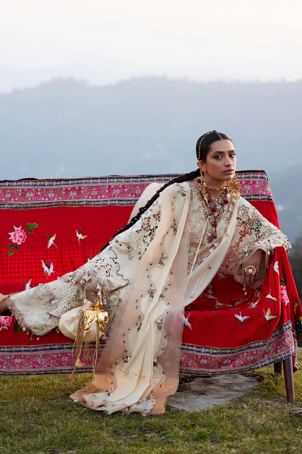 Woman in traditional attire sitting on a red and pink embroidered chair with mountains in the background