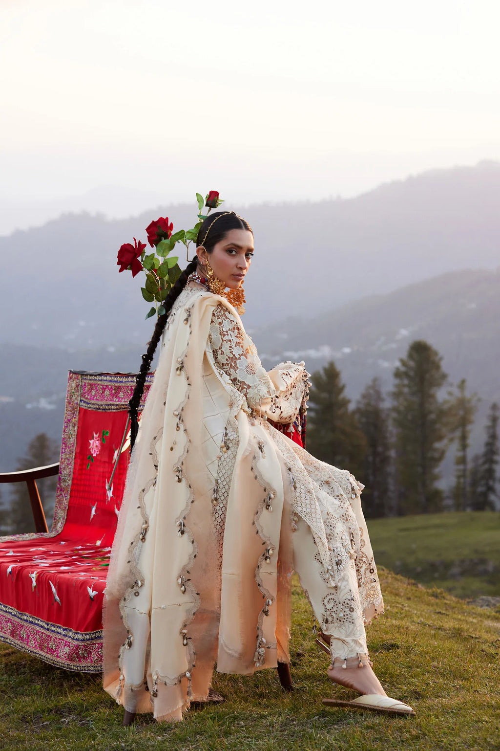 Woman in traditional attire standing next to a colorful chair with a mountainous background