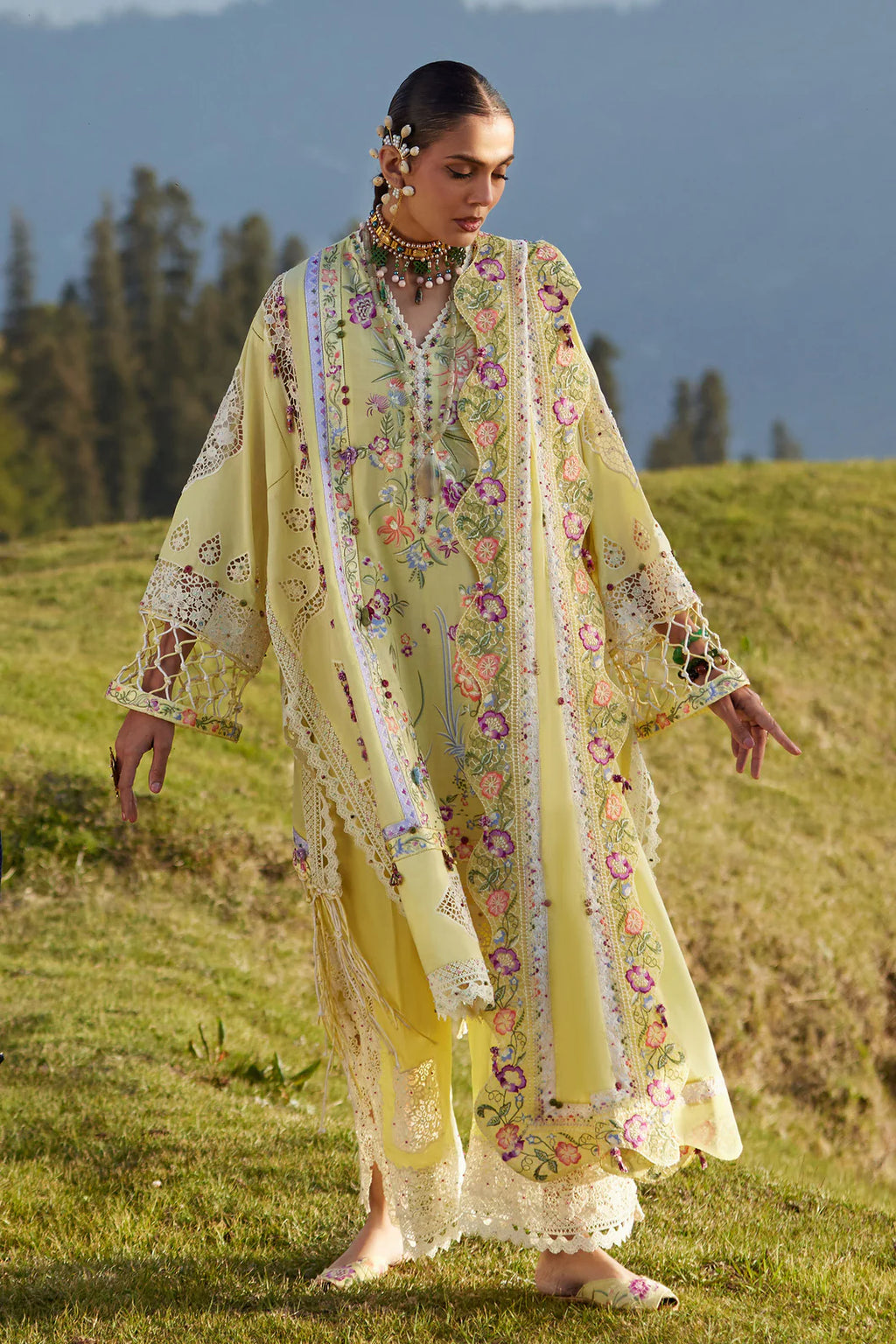 Woman in a floral dress standing in a grassy field with mountains in the background
