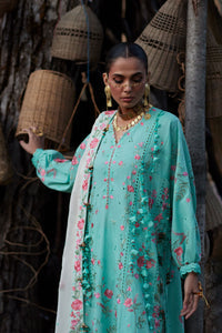 Woman wearing a turquoise floral dress with a matching dupatta in a rustic setting.