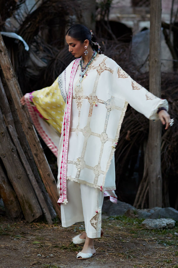 Woman in traditional white outfit with floral patterns standing outdoors.