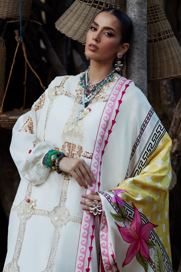 Woman in traditional outfit with floral patterns and jewelry, standing against a textured wall.