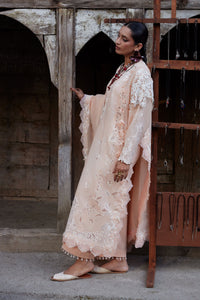 Woman in a beige lace dress standing in front of a rustic wooden door.