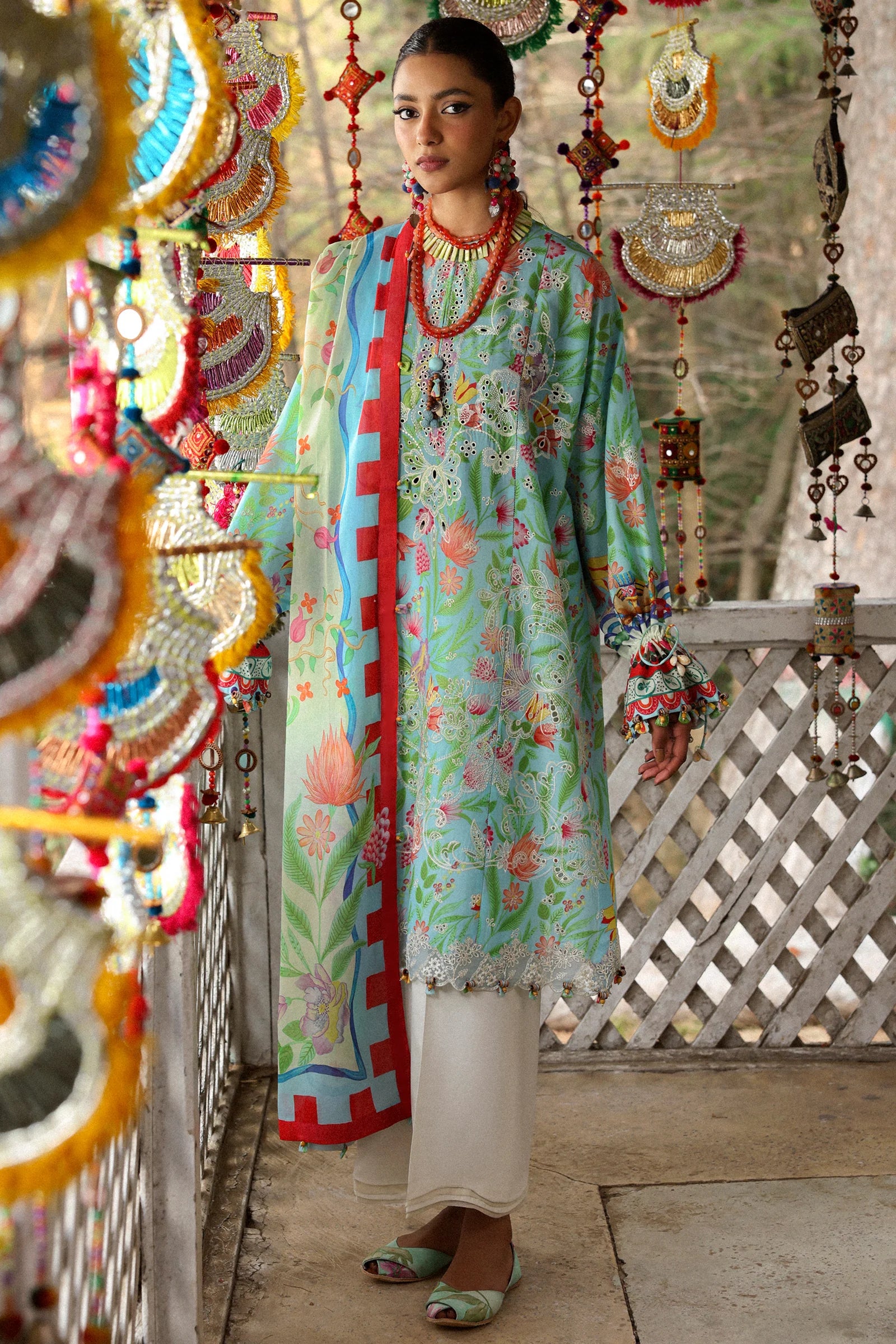 Woman in a colorful traditional outfit standing on a wooden deck with decorative hanging elements.