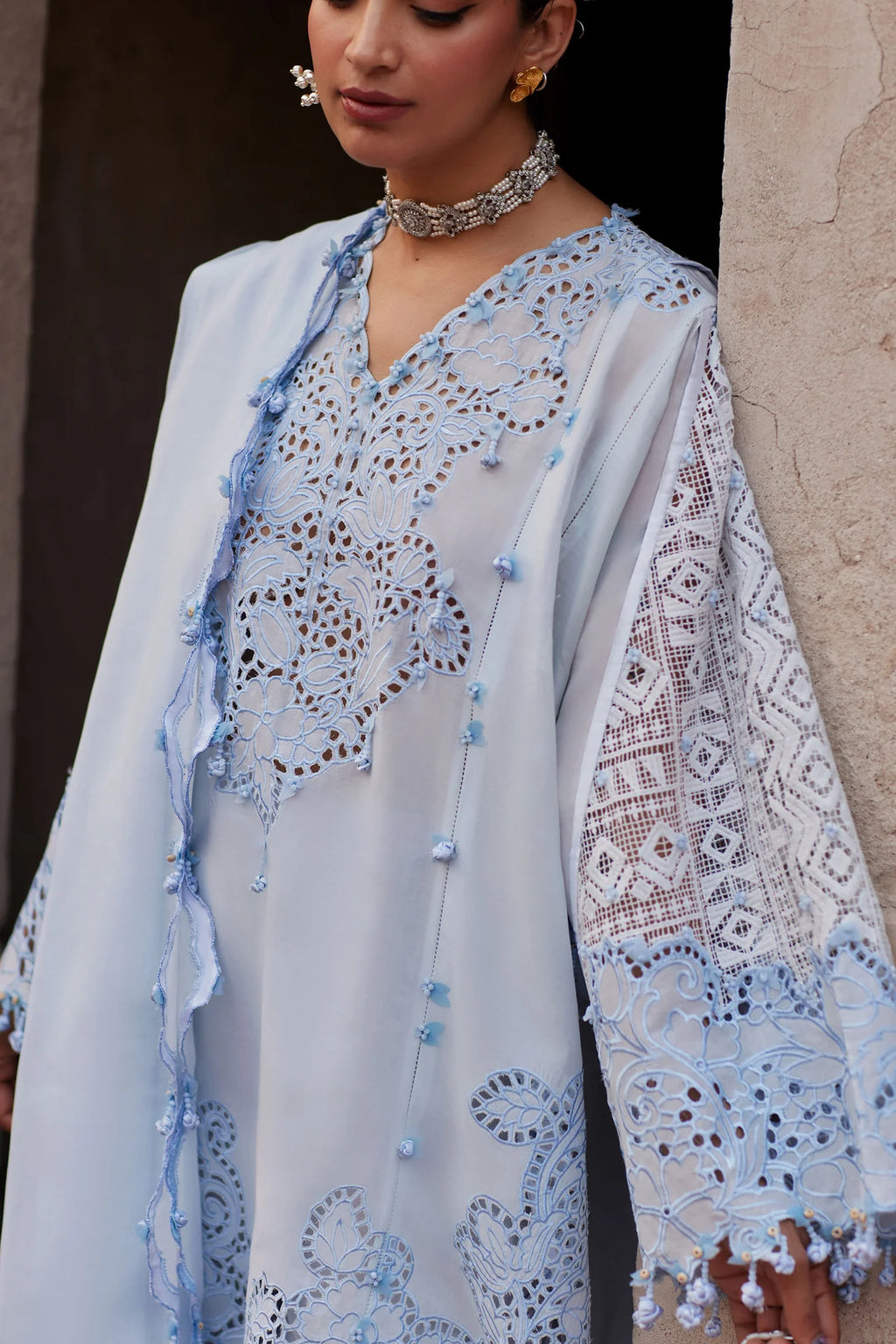 Woman wearing a light blue embroidered outfit with a textured wall background