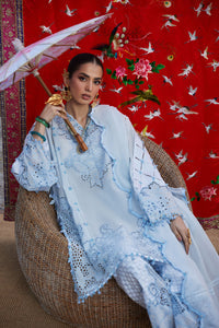 Woman in a light blue embroidered outfit holding a pink umbrella against a red floral background