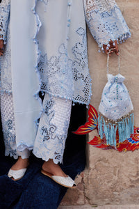 Person wearing a light blue embroidered outfit with a matching handbag against a stone wall.