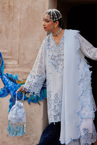Woman in traditional attire with a decorative headpiece and blue and white outfit, standing against a stone wall.