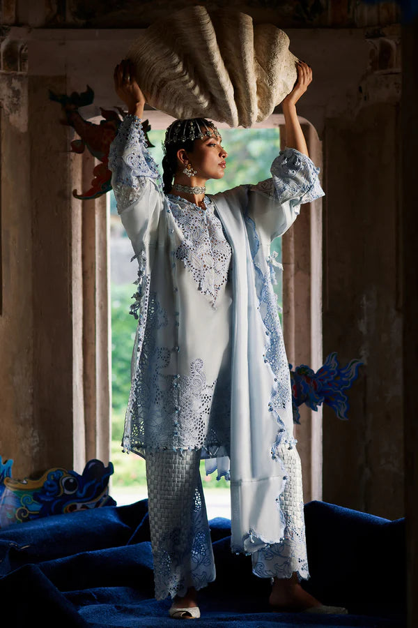 Woman in a light blue traditional outfit standing in a room with large windows.