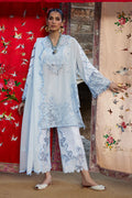 Woman in a light blue embroidered outfit standing in front of a colorful floral and bird patterned backdrop.