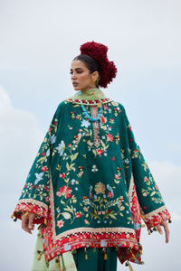 Woman wearing a green embroidered traditional outfit with a red and gold border against a light blue sky.