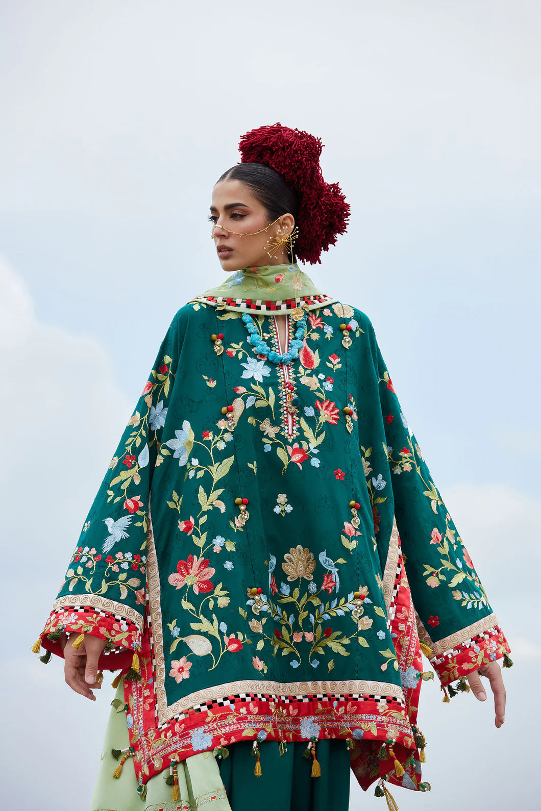 Woman wearing a green embroidered traditional outfit with a floral pattern against a light background