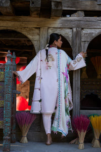 Woman in traditional attire standing in front of a wooden architectural structure with incense sticks.