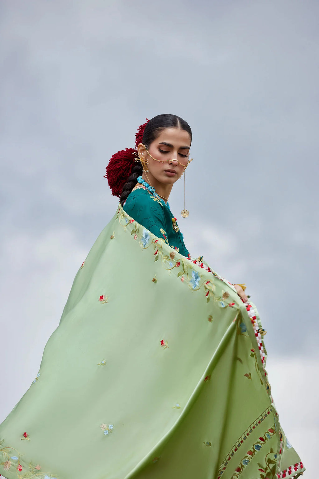 Woman wrapped in a light green floral shawl against a cloudy sky