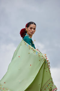 Woman wrapped in a light green floral shawl against a cloudy sky