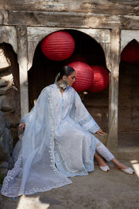 Woman in a light blue traditional outfit sitting in front of red lanterns.